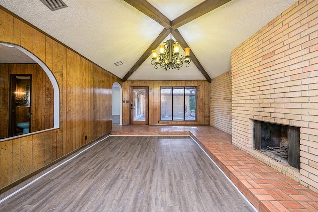 unfurnished living room with hardwood / wood-style floors, wooden walls, an inviting chandelier, and a textured ceiling