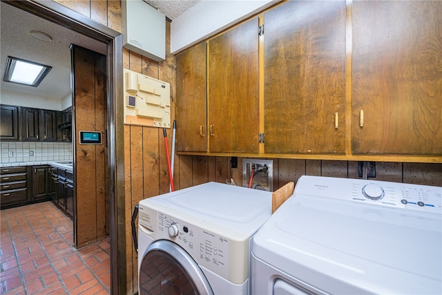 clothes washing area featuring cabinets, wooden walls, and separate washer and dryer