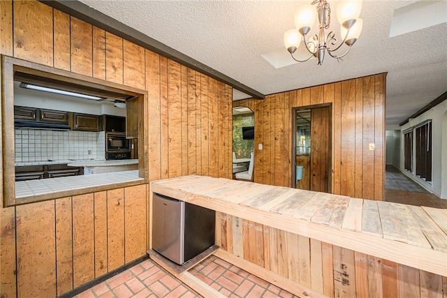 kitchen featuring an inviting chandelier, wooden walls, decorative backsplash, and stainless steel refrigerator