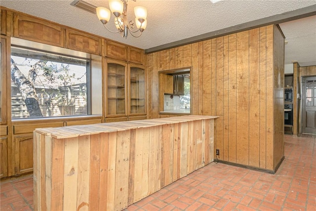 743 Retama Ave, Taft, TX 78390 - bar area featuring wood walls, black appliances, a chandelier, a textured ceiling, and brick floors
