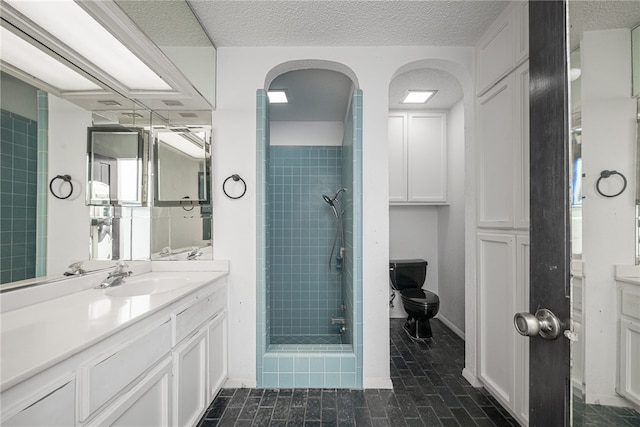 bathroom featuring toilet, vanity, a textured ceiling, and a tile shower