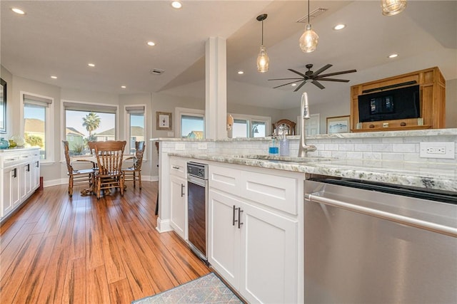 kitchen featuring pendant lighting, tasteful backsplash, white cabinets, stainless steel dishwasher, and light stone counters