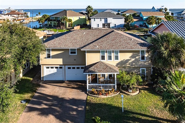 view of front of home with a water view, a garage, covered porch, and a front lawn