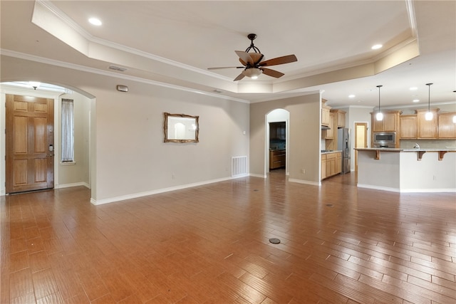 unfurnished living room featuring ceiling fan, dark hardwood / wood-style floors, crown molding, and a tray ceiling