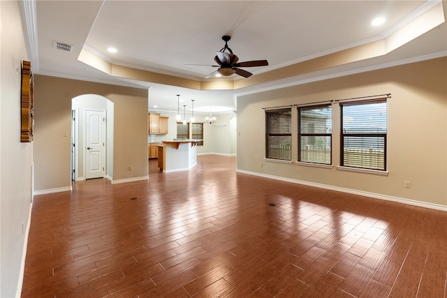 unfurnished living room featuring a tray ceiling, hardwood / wood-style flooring, ornamental molding, and ceiling fan with notable chandelier