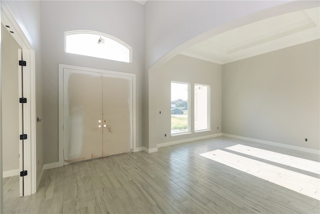 entryway with a high ceiling, a raised ceiling, light wood-type flooring, and crown molding