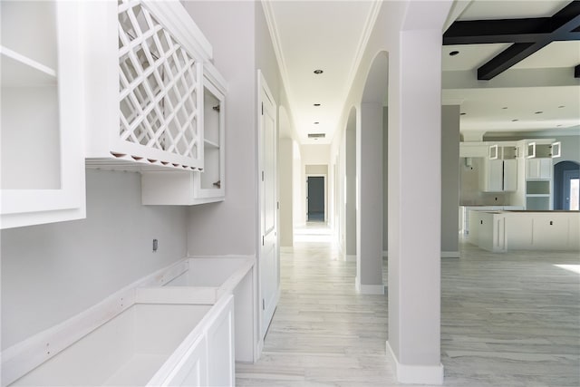 corridor with light wood-type flooring, ornamental molding, and beam ceiling