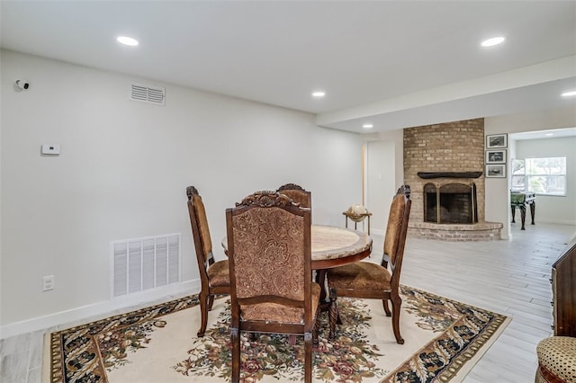 dining space featuring light wood finished floors, a brick fireplace, visible vents, and recessed lighting