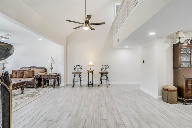 living area with ceiling fan, a high ceiling, baseboards, and light wood-style flooring