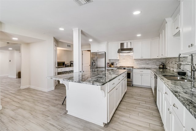 kitchen featuring appliances with stainless steel finishes, a sink, a kitchen island, dark stone countertops, and a kitchen breakfast bar