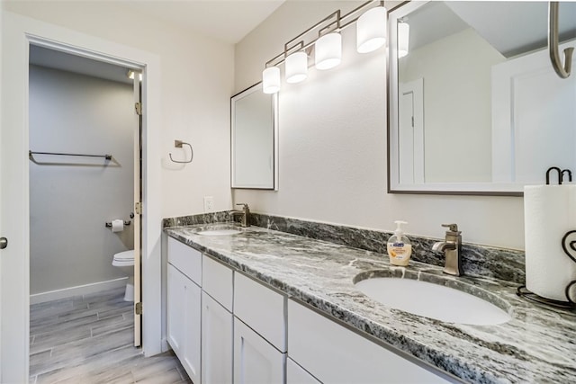 full bathroom with double vanity, wood finished floors, a sink, and toilet