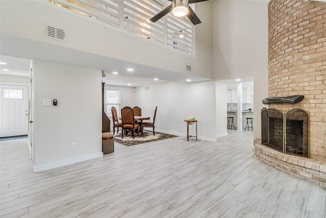 living area with baseboards, a brick fireplace, visible vents, and light wood-style floors