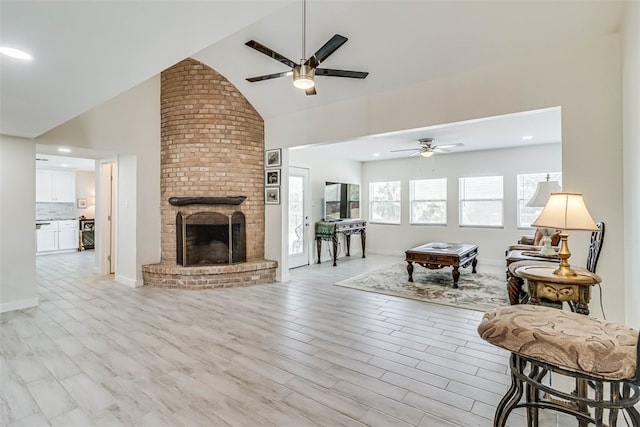 living area featuring high vaulted ceiling, light wood finished floors, a brick fireplace, and a ceiling fan