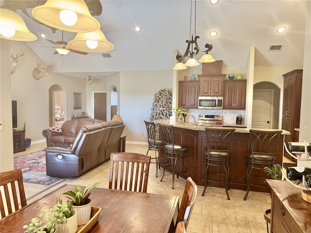 dining room with light tile patterned floors, ceiling fan with notable chandelier, lofted ceiling, and sink