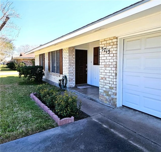 property entrance with a garage, a yard, and brick siding