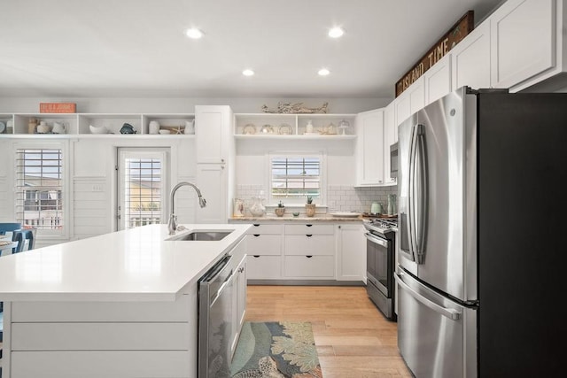 kitchen with a sink, light countertops, appliances with stainless steel finishes, open shelves, and an island with sink