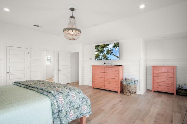 bedroom featuring lofted ceiling, light wood-style flooring, visible vents, and wainscoting