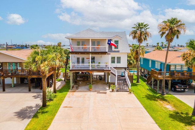 coastal inspired home with a shingled roof, stairway, a balcony, a carport, and driveway