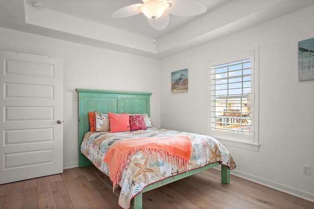 bedroom with a ceiling fan, baseboards, a tray ceiling, and wood finished floors