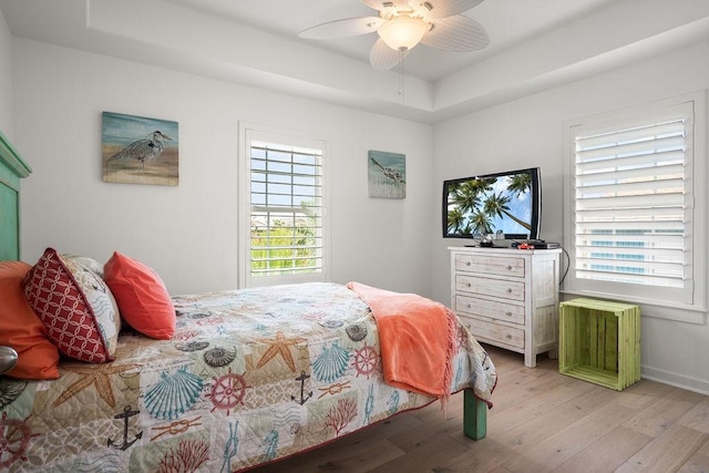 bedroom featuring a ceiling fan, a tray ceiling, and light wood finished floors