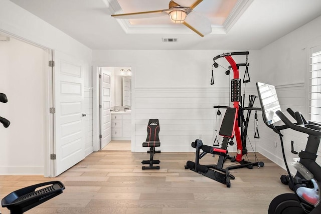 exercise area with light wood-type flooring, a raised ceiling, visible vents, and ceiling fan