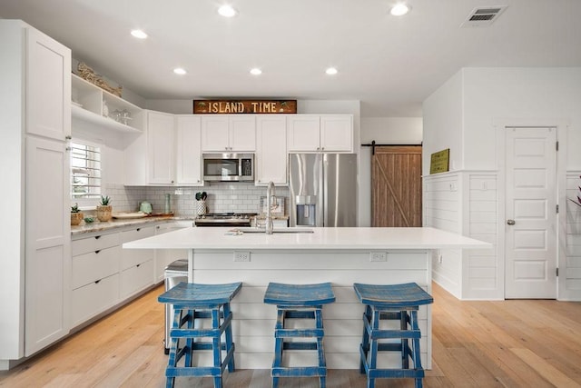 kitchen featuring a breakfast bar, visible vents, light countertops, appliances with stainless steel finishes, and an island with sink