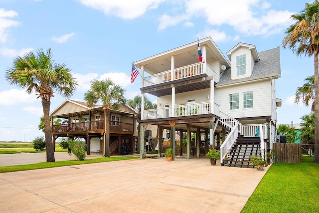 raised beach house with driveway, a shingled roof, a balcony, stairway, and a carport