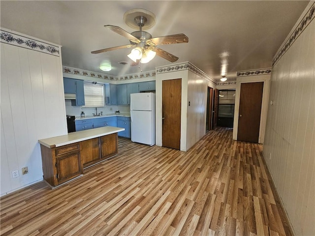 kitchen featuring light countertops, freestanding refrigerator, wood finished floors, blue cabinets, and a peninsula