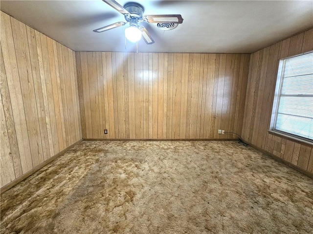 carpeted spare room with baseboards, a ceiling fan, and wooden walls