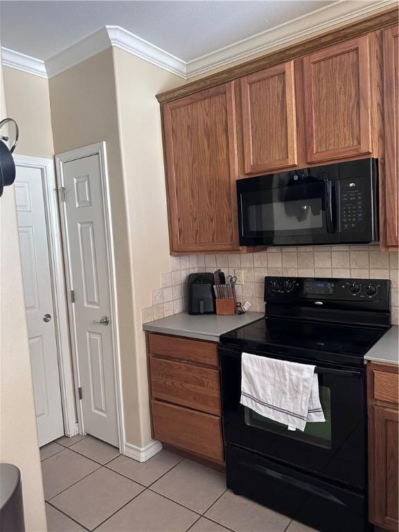 kitchen featuring brown cabinets, black appliances, ornamental molding, tasteful backsplash, and light tile patterned floors