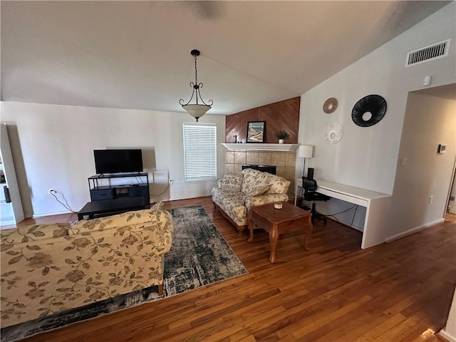 living area featuring a fireplace, vaulted ceiling, wood finished floors, and visible vents