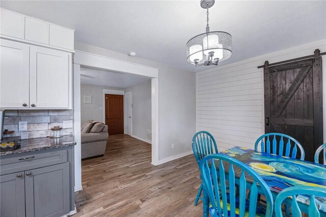 110 Wildwood, Rockport, TX 78382 - dining space with a barn door, a chandelier, light wood-style floors, wood walls, and a textured ceiling