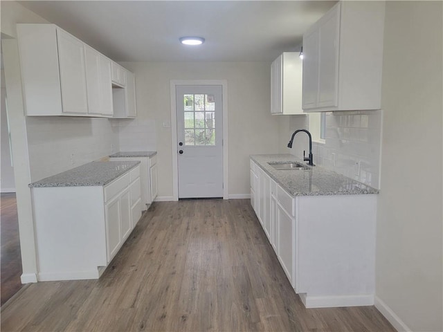 kitchen with light wood-type flooring, light stone counters, white cabinetry, and sink