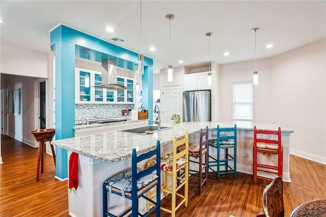 kitchen featuring sink, stainless steel refrigerator, a kitchen breakfast bar, range hood, and white cabinets