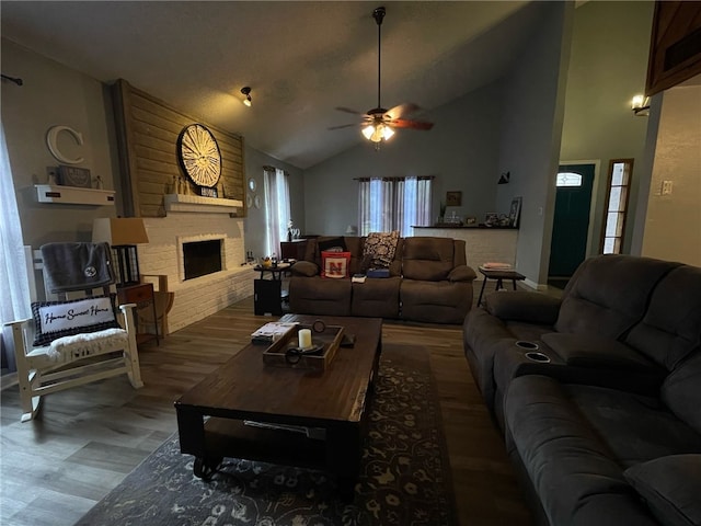 living room featuring lofted ceiling, a ceiling fan, a brick fireplace, and wood finished floors