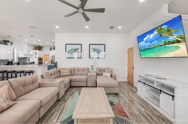 living room featuring ceiling fan, sink, and light wood-type flooring