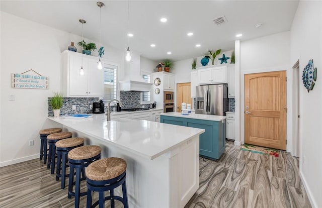 kitchen with white cabinetry, kitchen peninsula, a kitchen island, pendant lighting, and stainless steel appliances