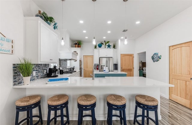 kitchen with appliances with stainless steel finishes, kitchen peninsula, white cabinets, and decorative light fixtures