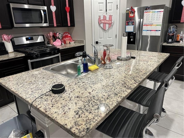 kitchen with appliances with stainless steel finishes, a kitchen breakfast bar, light stone counters, an island with sink, and light tile patterned flooring