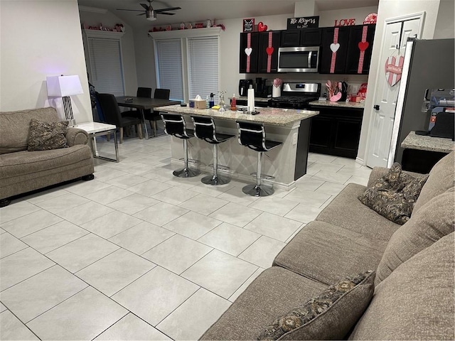 kitchen featuring light stone countertops, a kitchen breakfast bar, stainless steel appliances, ceiling fan, and a kitchen island