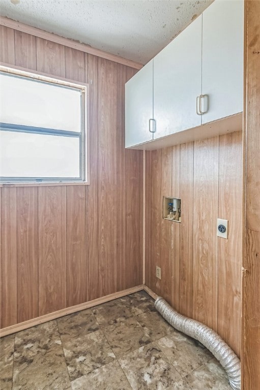 laundry area featuring electric dryer hookup, wood walls, cabinet space, and a textured ceiling