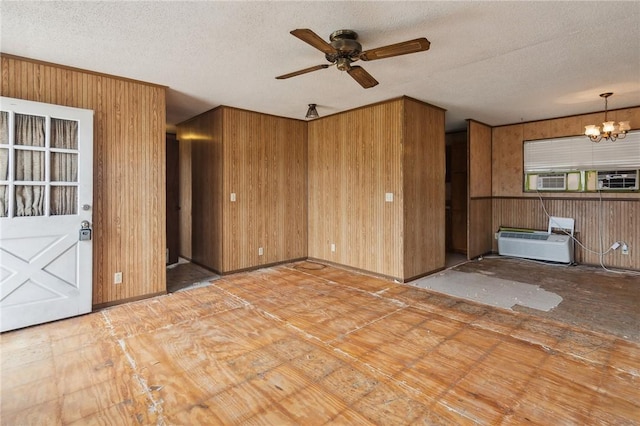 unfurnished living room featuring wooden walls, an AC wall unit, a textured ceiling, cooling unit, and ceiling fan with notable chandelier