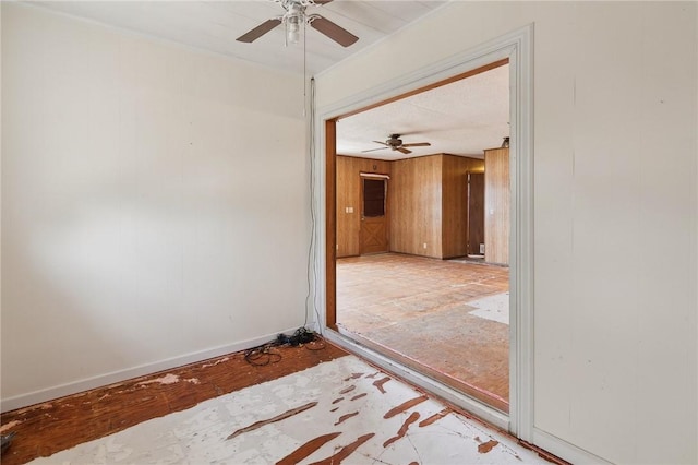 empty room featuring baseboards, wood walls, and ceiling fan