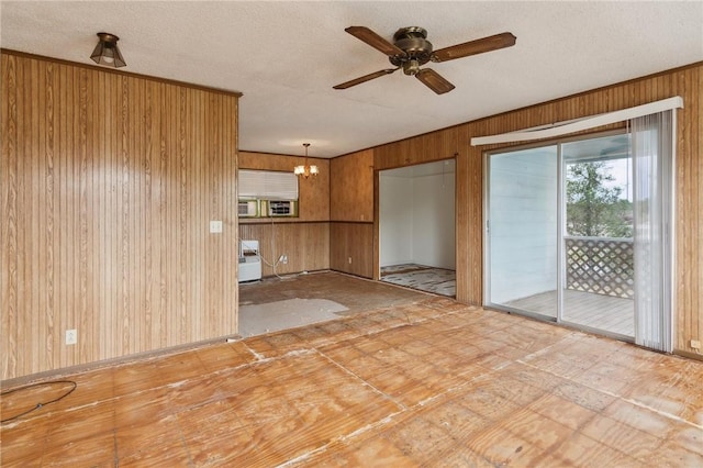 unfurnished living room with baseboards, ceiling fan with notable chandelier, wood walls, and a textured ceiling