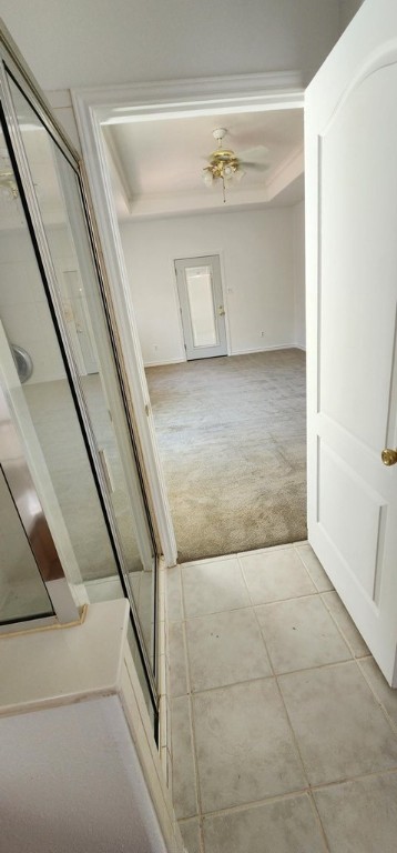 corridor with ornamental molding, light colored carpet, and a tray ceiling