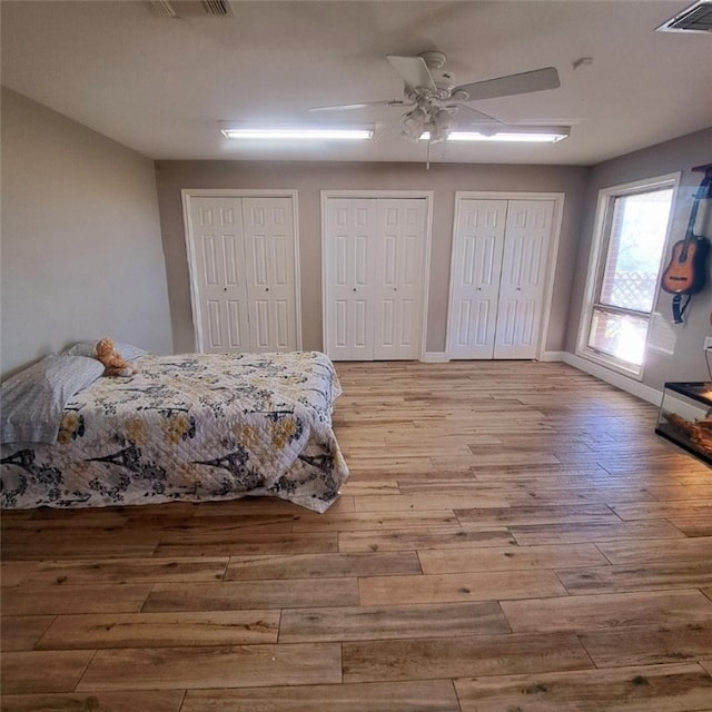 bedroom featuring ceiling fan, multiple closets, and light hardwood / wood-style flooring