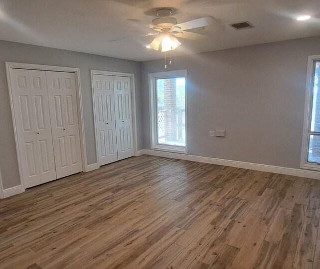 unfurnished bedroom with hardwood / wood-style floors, ceiling fan, and multiple closets