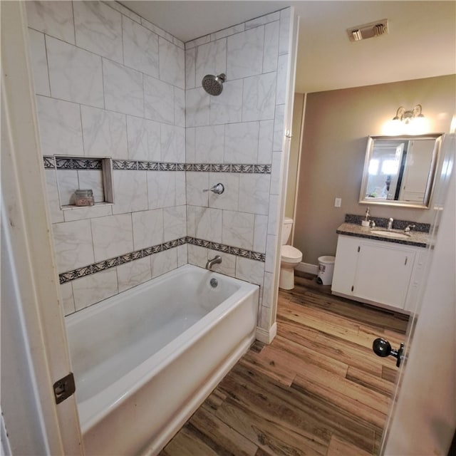 full bathroom featuring hardwood / wood-style flooring, tiled shower / bath combo, toilet, and vanity