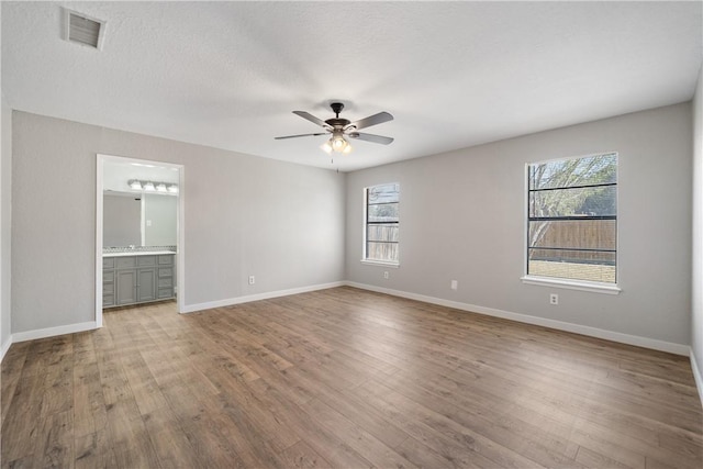 empty room featuring a textured ceiling, wood finished floors, visible vents, baseboards, and a ceiling fan