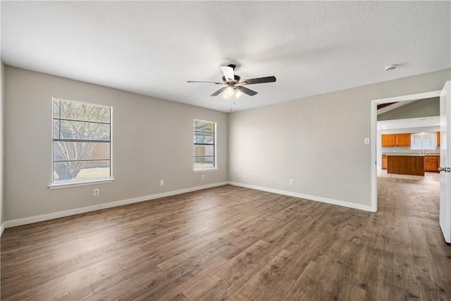 empty room with ceiling fan, a textured ceiling, baseboards, and wood finished floors